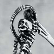 Close-up of the lower part of the skull scythe pendant, showing the handle with bone-like details held by fingers.