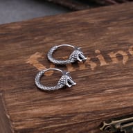 Pair of stainless steel Viking wolf head hoop earrings resting on a wooden box