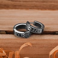 Pair of stainless steel Viking wolf head hoop earrings with rune carvings on a wooden surface
