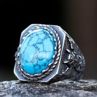 Viking raven stainless steel ring with turquoise cabochon center resting on stone