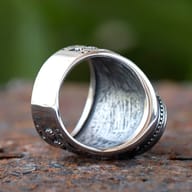 Oblique shot highlighting the textured surface and black stone of the steel ring.