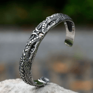 Oxidized stainless steel cuff bracelet featuring detailed dragon scales, multiple recessed dragon eyes, and a small red accent.