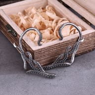 Pair of stainless steel kraken tentacle earrings displayed against a rustic wooden box