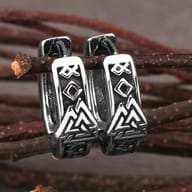 Pair of stainless steel Viking Valknut hoop earrings resting on rustic wooden twigs