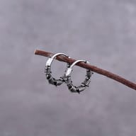 Pair of gothic barbed wire stainless steel hoop earrings hanging on a twig against a gray background