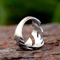 Side view of the flame-inspired stainless steel ring, showcasing its dynamic open design on a textured brown surface.