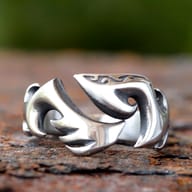 Close-up of a gleaming silver-toned stainless steel flame-inspired open ring on a rustic, rusty surface.