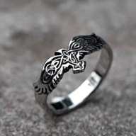 A men's polished and oxidized stainless steel ring featuring a detailed Viking eagle design with intricate Celtic knotwork, presented on a gray concrete surface.