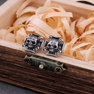 Pair of gothic skull iron cross stud earrings resting on a wooden box edge