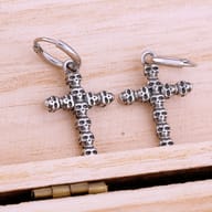 Pair of stainless steel gothic skull cross drop hoop earrings resting on light wood