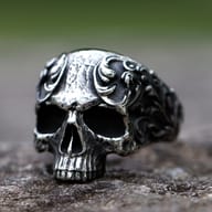 Close-up of a vintage gothic skull ring crafted from 316L stainless steel, featuring intricate scrollwork on a textured stone surface.