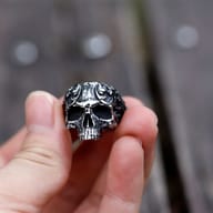 Angled close-up showcasing the side profile and elaborate scroll designs of the men's skull ring.