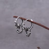 Pair of 316L stainless steel spiked hoop earrings resting on a textured dark background