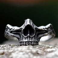Close-up of a vintage gothic steel skull ring on a textured rock surface.