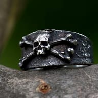 Close-up of a vintage 316L stainless steel men's ring featuring a skull and crossbones design, resting on a rustic wooden surface.