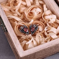 Detailed front view of a gothic bat wing skull earring with an oval red crystal center