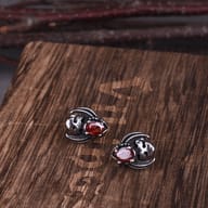 Flat lay view of gothic skull and wing earrings with red faceted stones on a textured dark surface