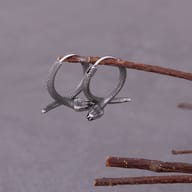 Pair of textured 316L stainless steel coiled snake hoop earrings suspended from a rustic twig