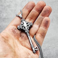 Detail of the top ornate section of the stainless steel key pendant against a grey background