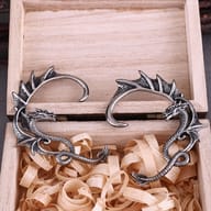 Pair of stainless steel flying dragon ear wrap earrings resting in a wooden display box