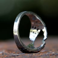 Angled view of the 316L stainless steel skeleton hand heart ring, emphasizing its sculpted design and dark antique finish on a rustic background.
