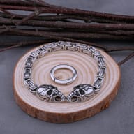 Men's stainless steel Byzantine chain bracelet with dual gothic skulls and spring ring clasp on wooden display