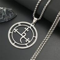 Close-up of the top of the 316L stainless steel Lilith seal pendant and bail, with the chain resting on a dark, rocky surface.