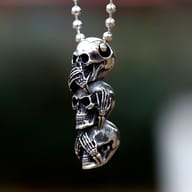 Close-up of the skeletal hands covering eyes, ears, and mouth on skull pendant