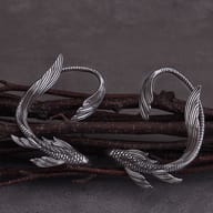 Pair of stainless steel koi fish ear wrap cuffs resting on rustic dark branches