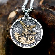 Close-up of the top right of the St. Michael pendant and chain on a textured surface.