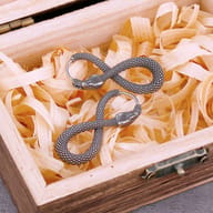 Close-up of the left snake earring's head and hoop closure against a light wood background.