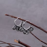 A pair of 316L stainless steel snake hoop earrings hanging from a rustic tree branch against a blurred grey background.