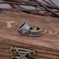 Pair of stainless steel Viking rune ear cuffs resting on a rustic wooden box