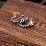 Pair of vintage stainless steel dragon hoop earrings resting on a wooden box
