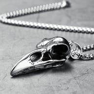 Gothic crow skull pendant's elongated beak and eye socket held by a finger, showing its distinct shape.