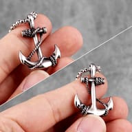 Angled view of the stainless steel anchor pendant on a gray surface, showcasing its three-dimensional design.