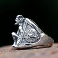 Top-down view of men's fallen angel steel ring resting on a textured dark surface