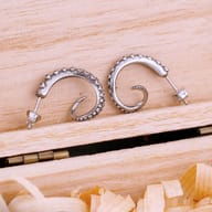 Top angle of both 316L stainless steel tentacle earrings on decorative wood shavings