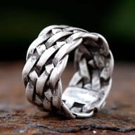 Close-up of an antiqued 316L stainless steel ring with a wide, woven braided chain design, set against a dark, rustic background.
