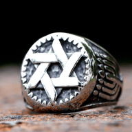 A shiny stainless steel ring features a raised hexagram on a textured dark background, bordered by a serrated edge, with patterned designs on the sides.
