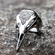 Celtic knot raven skull stainless steel ring resting on a textured stone surface
