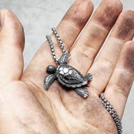 Angled view focusing on the polished and textured shell of the 316L stainless steel turtle pendant.