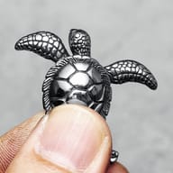Side profile of the 316L stainless steel turtle pendant on a finger, highlighting its dimensional design.