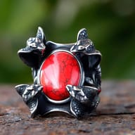 Close-up of a 316L stainless steel ring featuring four detailed snake heads surrounding a vibrant red zircon stone, set against a blurred green background.
