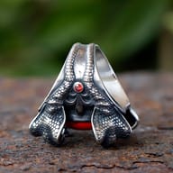 Frontal close-up highlighting the texture of the lower left snake head and the striking red zircon cabochon of the stainless steel ring.