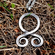 Front view of Viking troll cross pendant resting on natural dry grass with steel chain