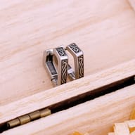 Pair of stainless steel geometric huggie hoop earrings with engraved Nordic patterns resting on wood