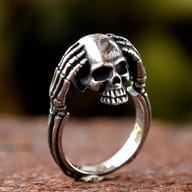 Front view of the skull design on the stainless steel ring, highlighting the detailed facial features and hand position.